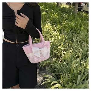 Detail of pink and white woven bucket bag with large bow in a natural outdoor setting
