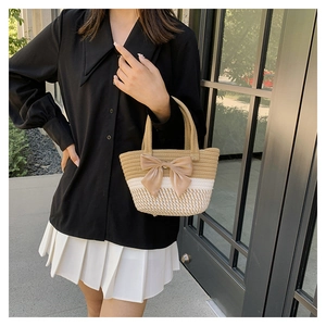 Detail of woven straw tote bag featuring contrast stitching and large bow decoration