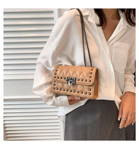 Close-up of khaki quilted crossbody bag with stud detailing and metal chain strap