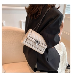 Rear view of a white quilted crossbody bag with metal rivets on a black blazer