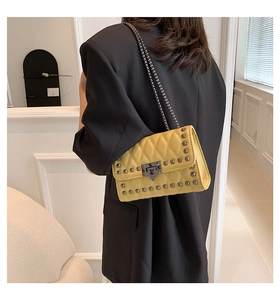 Model wearing a bright yellow quilted crossbody bag with studs and metal chain strap