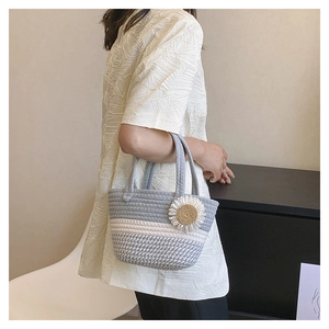 Detail of hand-woven striped knit bag with sunflower charm held by woman in white shirt