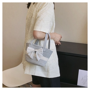 Close-up of handmade grey striped woven bag with large white ribbon bow decoration