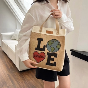 Chic jute tote bag with LOVE globe print and brown leather handles on a white sofa