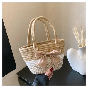 Detail of hand-woven beige and white striped bucket bag with a large champagne satin bow