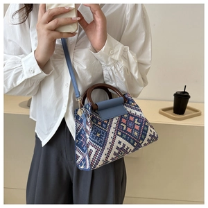 Detail of geometric woven crossbody bag with round wooden handles and blue leather flap