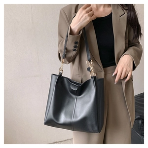 Detail of a black leather tote bag with gold chain strap on a brown blazer outfit