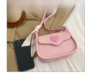 Rosa Umhängetasche mit Herzdetail neben einem Smartphone zum Größenvergleich