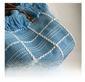 Detail of blue woven fabric with white grid pattern and bohemian fringe accents