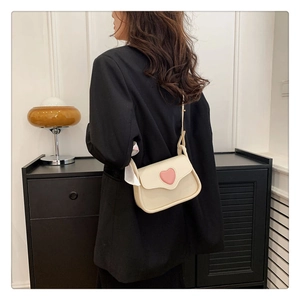 Seitenansicht der cremefarbenen Ledertasche mit pinkem Herz auf schwarzem Blazer