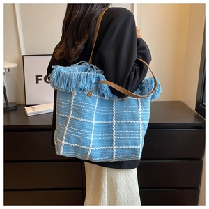 Detail of blue woven tote bag with fringe trim and brown leather handles on a model
