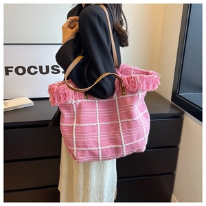Pink woven tote bag with white grid pattern and tassel trim shown on model