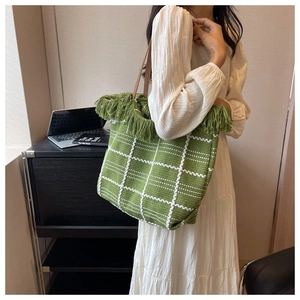 Detail of green woven tote bag with white checkers, fringe trim, and brown leather handles