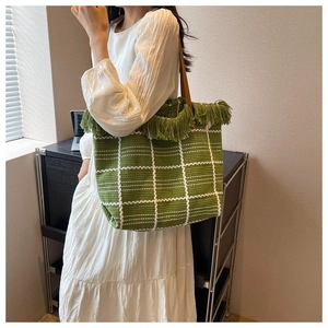 Detail of green woven tote bag with white grid pattern and green fringe tassels