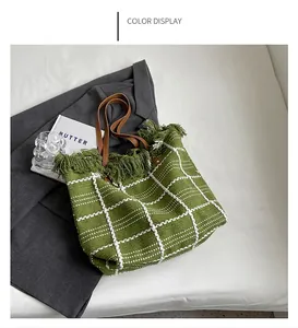 Grand sac cabas tressé vert avec franges et anses en cuir marron sur fond blanc