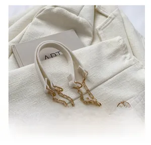 Dettaglio di tracolla bianco crema con tessuto felpato e maglie di catena in metallo dorato
