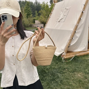 Mini borsa a secchiello in paglia con chiusura a perla e tracolla in un ambiente esterno