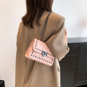 Pink quilted shoulder bag with studs and chain strap shown on a model in a brown suit