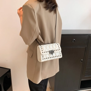 White quilted crossbody bag with metal studs and chain strap shown on model