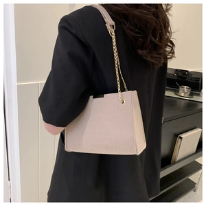 Dettaglio di una borsa a tracolla beige motivo coccodrillo con catena d'oro su una modella