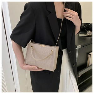 Dettaglio di una borsa beige effetto coccodrillo con tracolla a catena dorata su modella