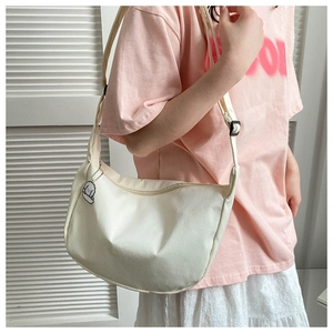 Détail d'un sac demi-lune en toile beige avec porte-clés chien et bandoulière réglable