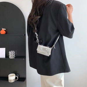 Mini silver metallic square crossbody bag with acrylic chain worn by a model in a black suit