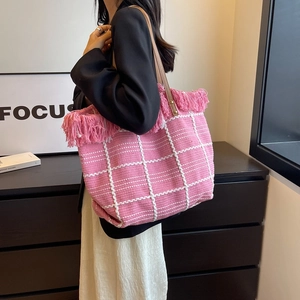 Pink woven tote bag with white grid pattern, stylish fringe trim, and brown leather handles