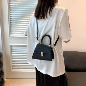 Minimalist black leather trapezoid handbag with gold buckle shown on a model
