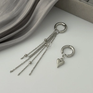 Détail de boucles d'oreilles argentées asymétriques avec cœur et chaînes métalliques