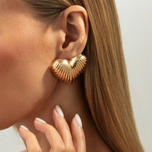Close-up of a gold heart earring with 3D pleated texture worn by a fashion model