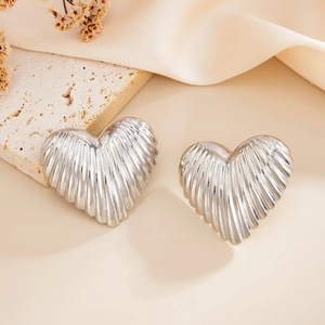 Detailed close-up of silver heart stud earrings with unique wrinkled metal texture on silk