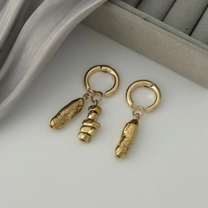 Détail de boucles d'oreilles dorées asymétriques avec texture martelée sur de la soie