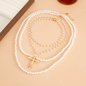 Détail de colliers de perles superposés avec un pendentif en croix dorée élégant