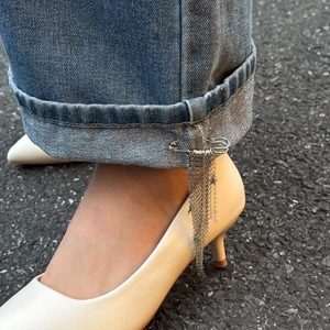 Close-up of star tassel chain brooch pinned to denim pants with high heels background