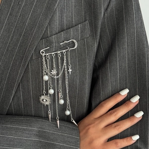 Silver safety pin brooch with metallic tassels, faux pearls and charms on a suit