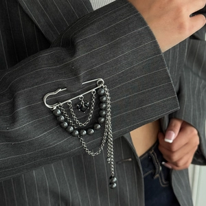 Detail of silver brooch pin with multi-layered metal chains and a black heart gem pendant