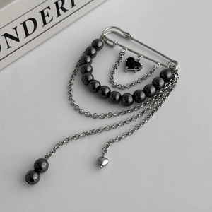 Detail of silver safety pin brooch with hanging chains, black beads and heart charms
