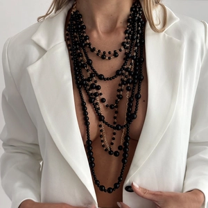 Close-up of layered black beaded long necklace with gold chain on a white blazer