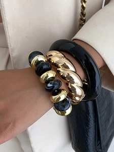 Detail of stacked gold twist bangle and black resin bracelets with marble bead bracelet