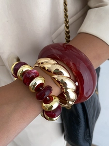 Close-up of stacked resin and gold metal bracelets on wrist with red marble beads