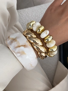 Detail of stacked gold twisted bangle and white marble resin bracelet on wrist