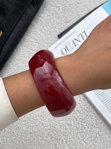 Detail of wide wine red resin bangle with glossy finish worn on wrist against magazine