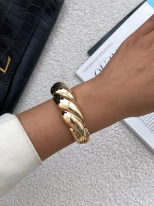 Detail of chunky gold twisted bangle with high-polish finish shown on model