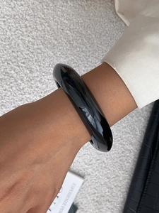 Close-up of a glossy wide black resin bangle paired with a beige blazer and leather bag