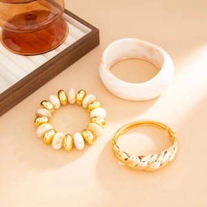 Detail of marble resin cuff and gold beaded bracelet on a warm minimalist background