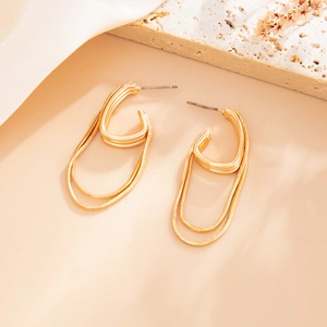 Detail of layered gold tassel earrings with sleek chain drops on a stone background