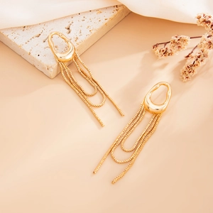 Detail of long gold tassel earrings with chain fringe on a textured stone background