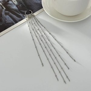 Detail showing silver tassel ear cuff with long metallic ball chains on a white surface
