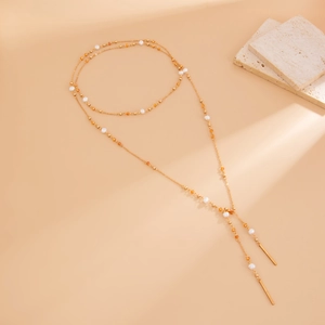 Detail view of long gold pearl necklace with orange beads and elegant tassel pendants
